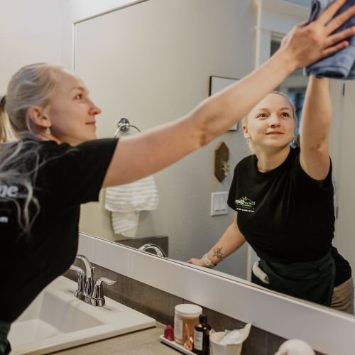 Rise and Shine female house cleaner wipes the bathroom mirror